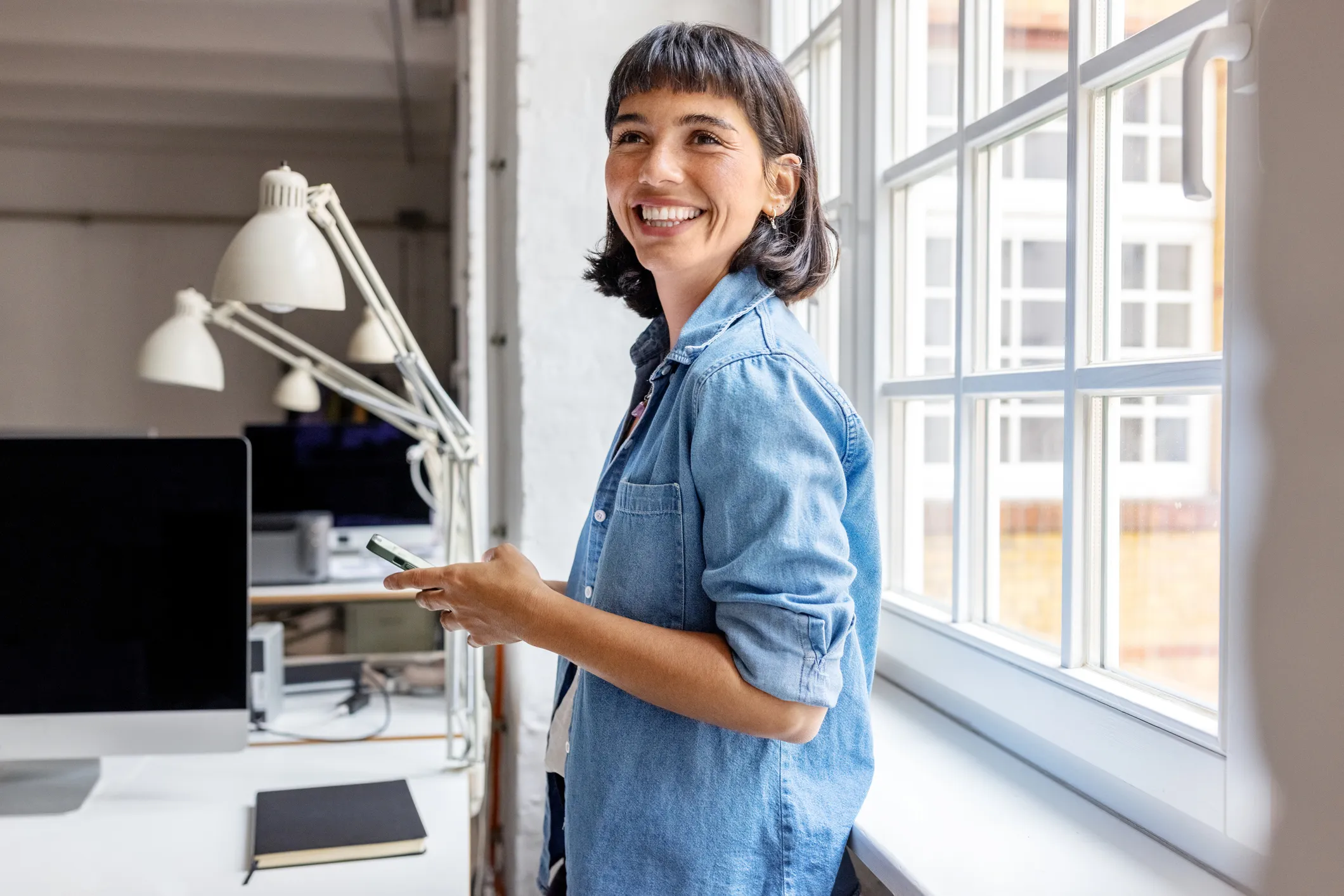 A woman standing in front of a window next to a computer.