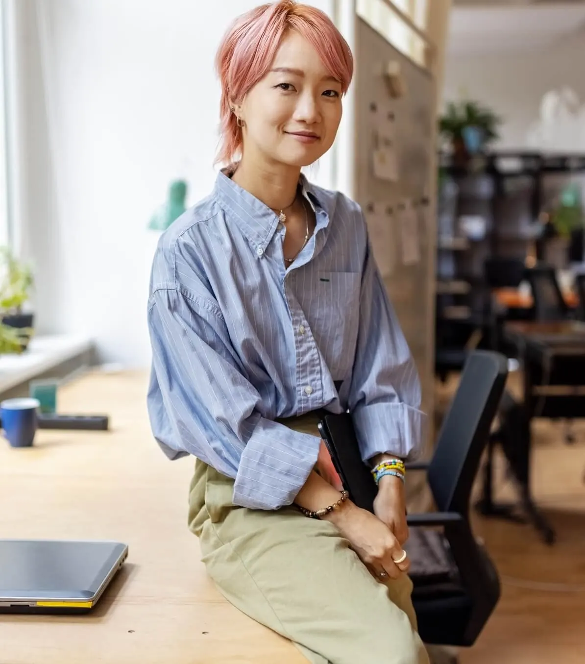 A woman with pink hair sitting on a desk.